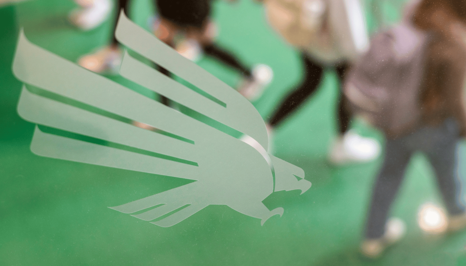 Group of Students walking past the eagle logo on glass