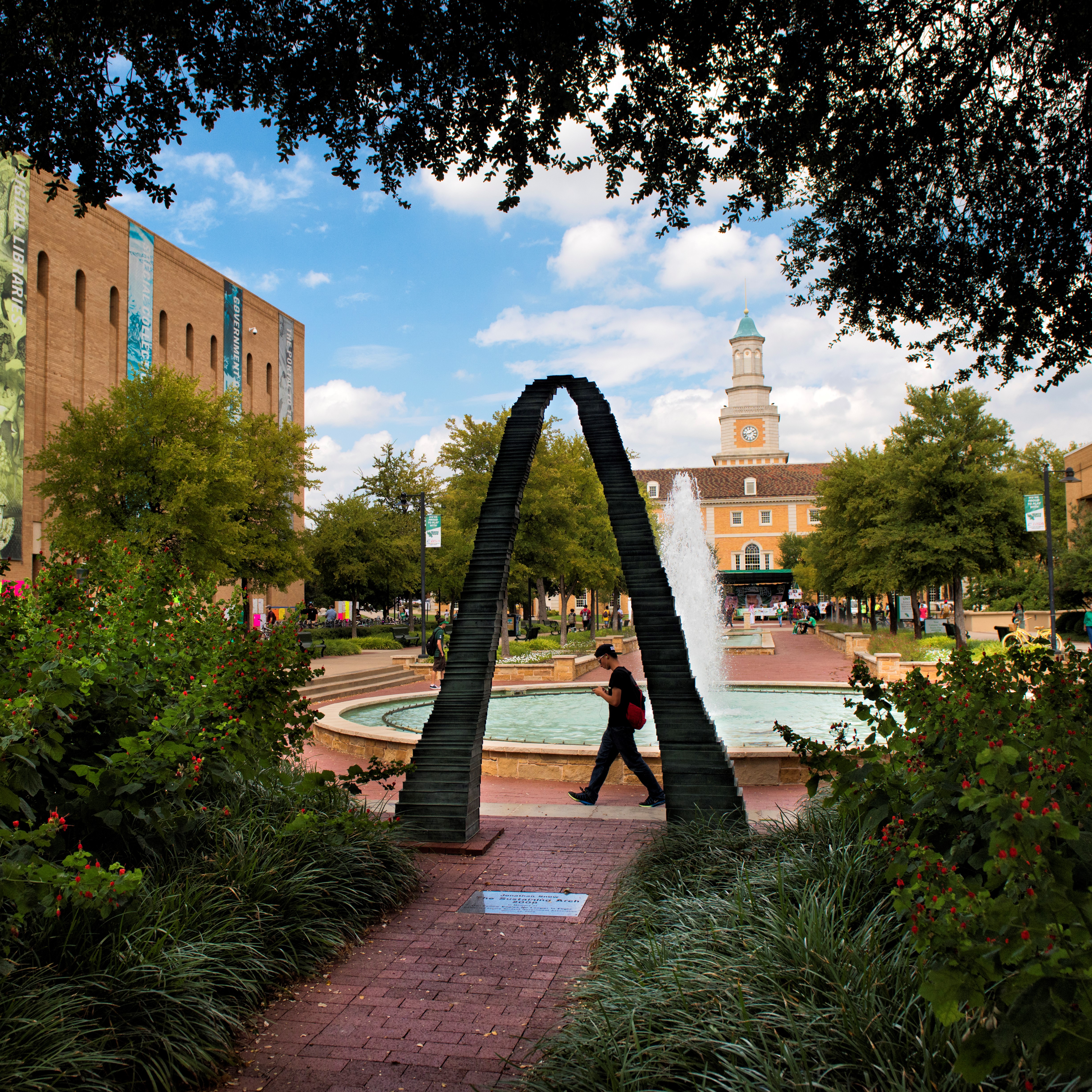 The arch out by the union mall fountain is shaded by trees over it.