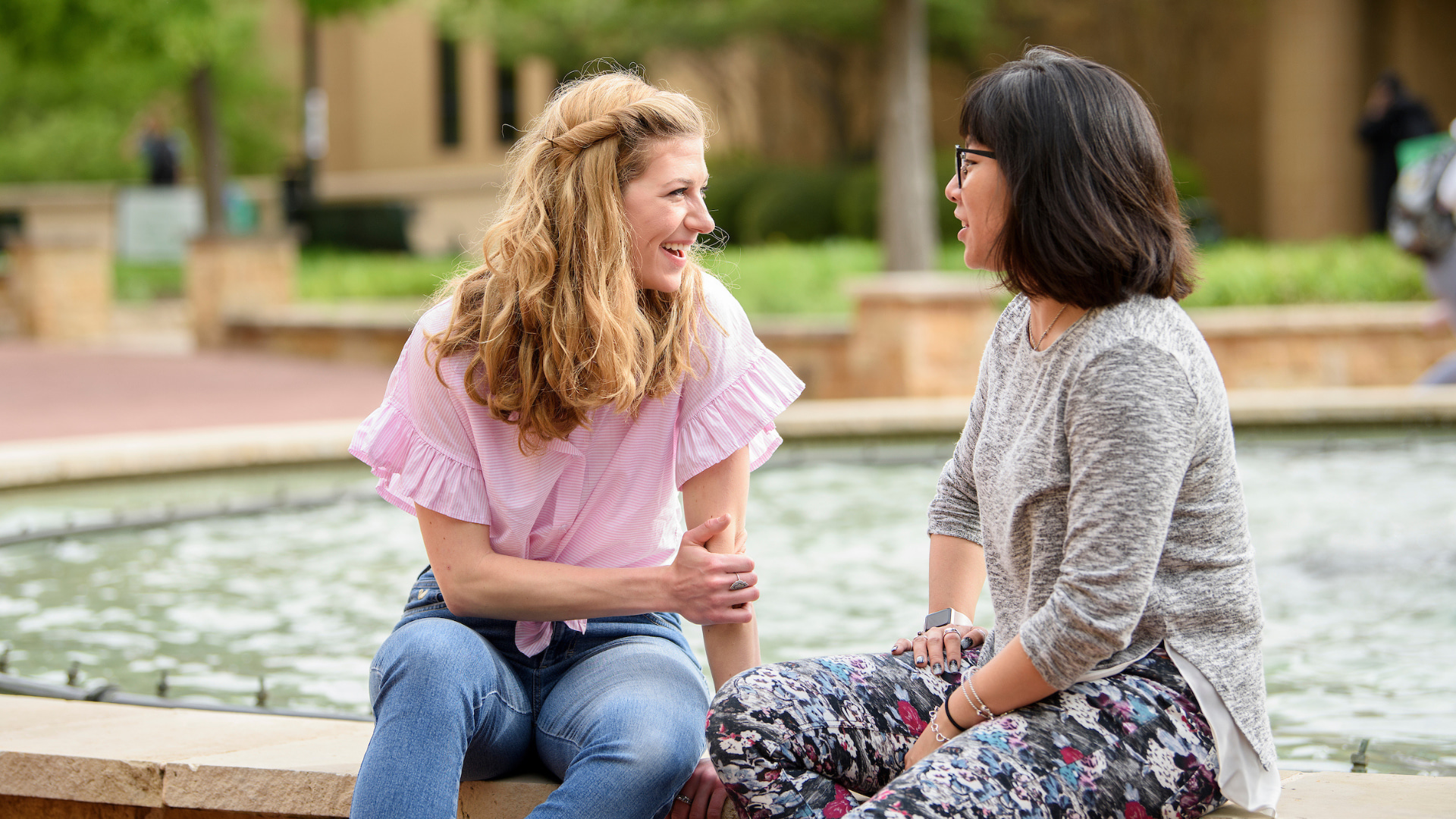 Two students smiling and sitting at the water fountain, talking