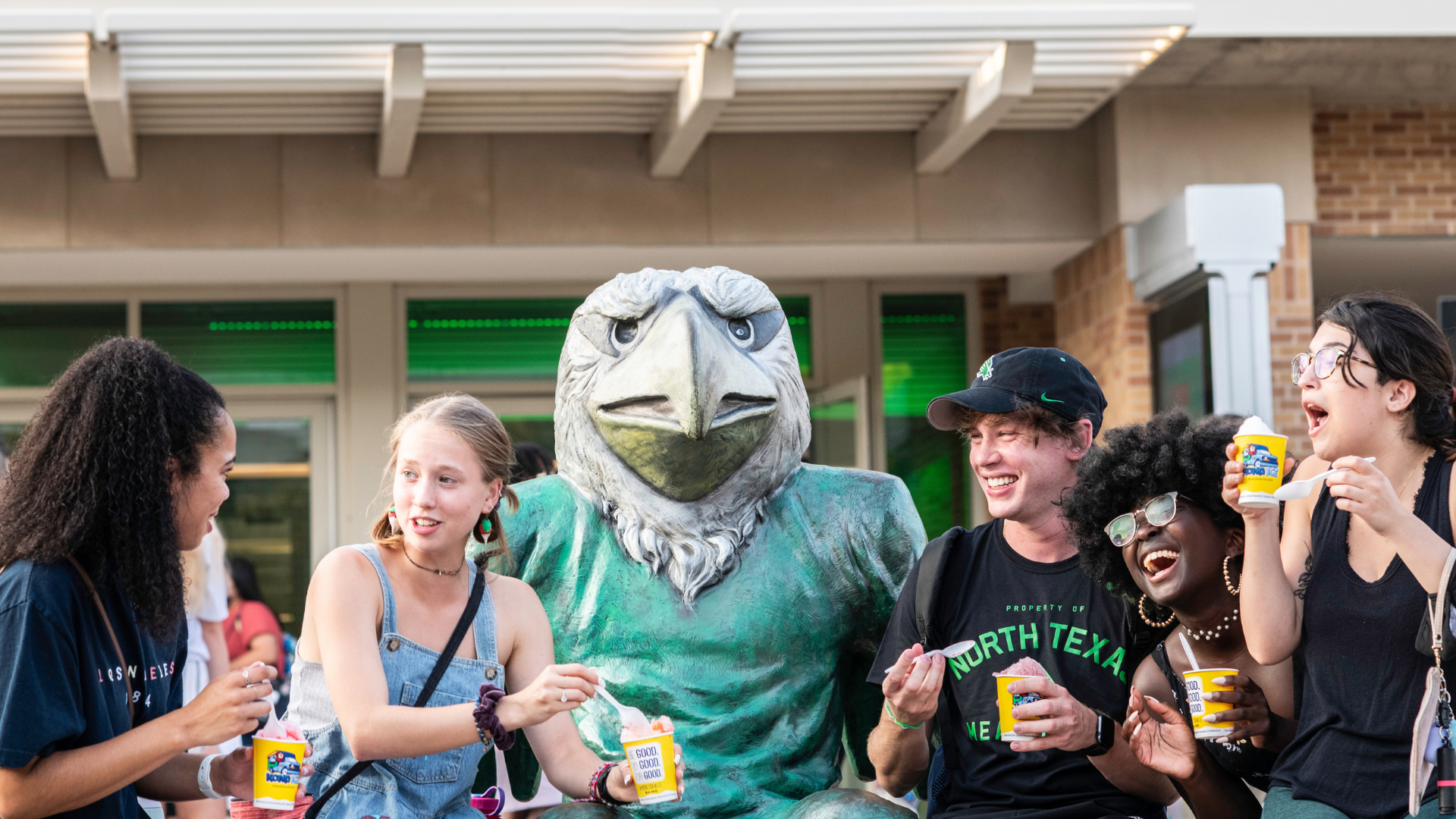 Group of students smiling as they eat snow cones next to the Scrappy statue