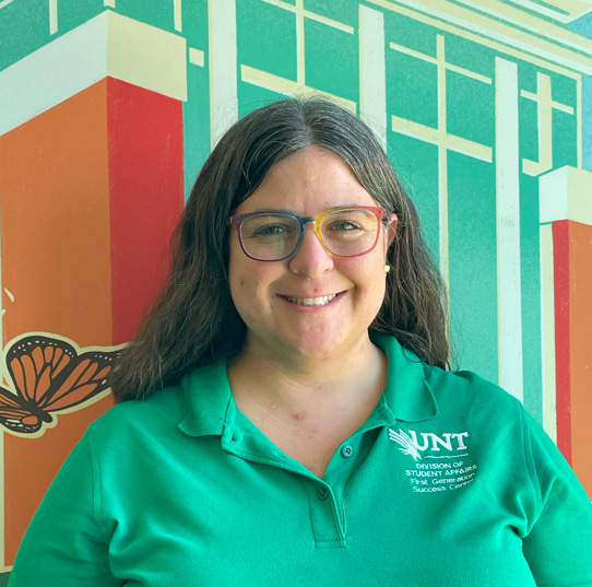 Photo of a woman in a green shirt smiling in front of a colorful mural.