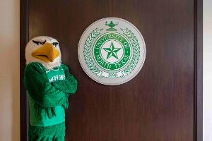 Scrappy stands next to the UNT seal.