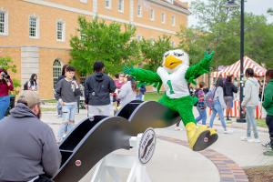 At the UNT carnival, Scrappy rides a seesaw with a student.