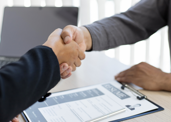 Two people sitting at desk shaking hands.