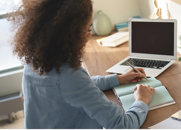 Student sitting at desk with laptop and notebook.