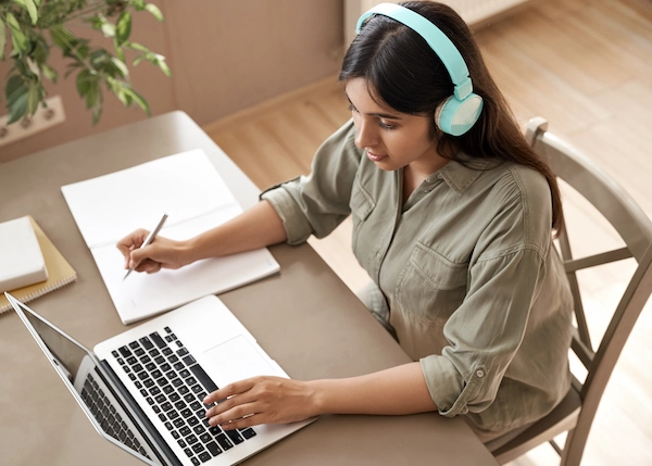 Student sitting at a desk with a laptop and notebook wearing headphones.