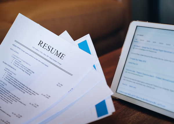 Person holding resume sitting at a table with a tablet device