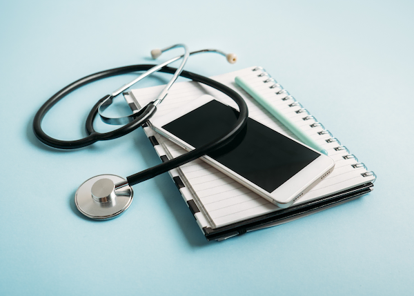 Photo of stethoscope, smartphone and notepad on blue background.