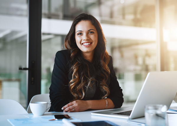 Woman sitting at a desk with a laptop smiling.