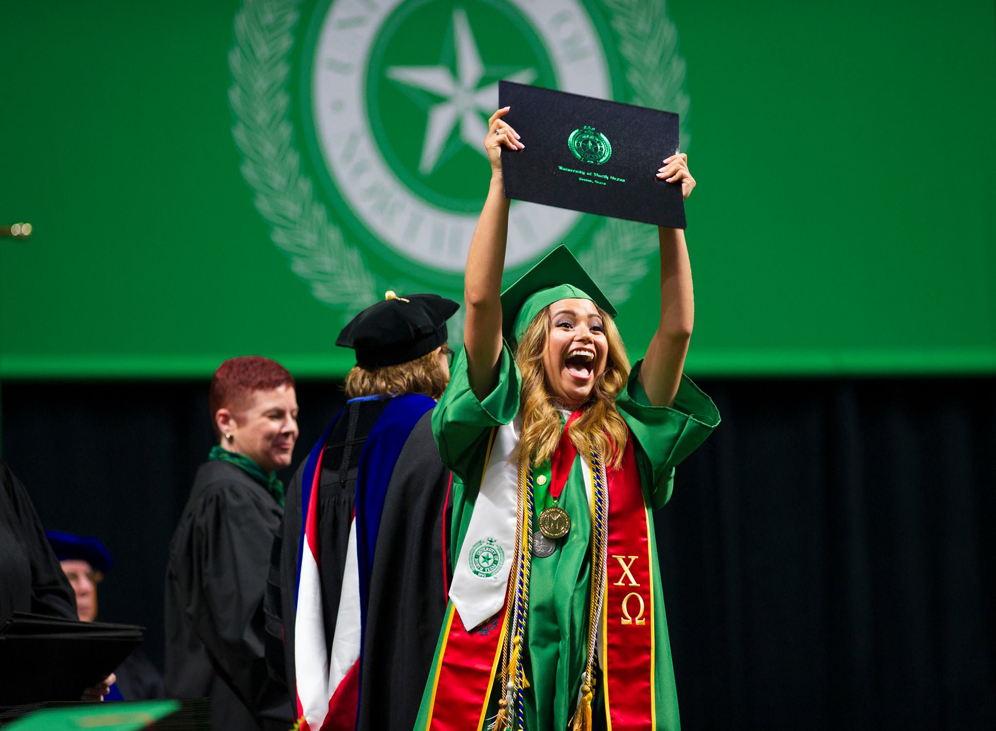 Graduating senior holding up diploma at Commencement. 