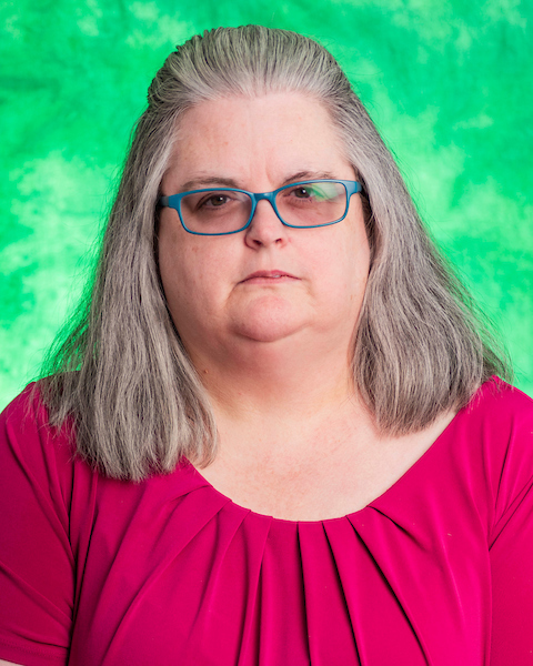person with glasses standing in front of green background