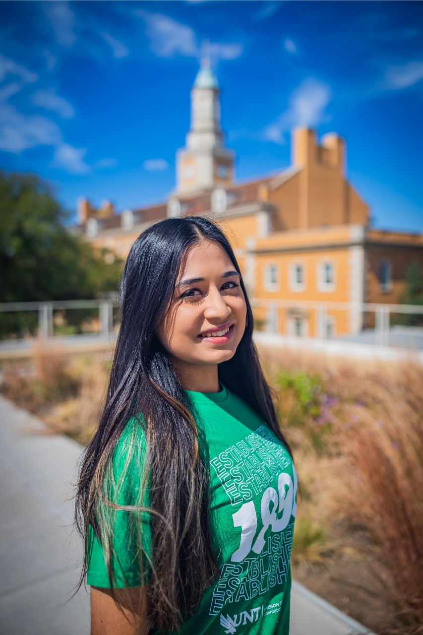 person with long hair in unt shirt infront of admin building