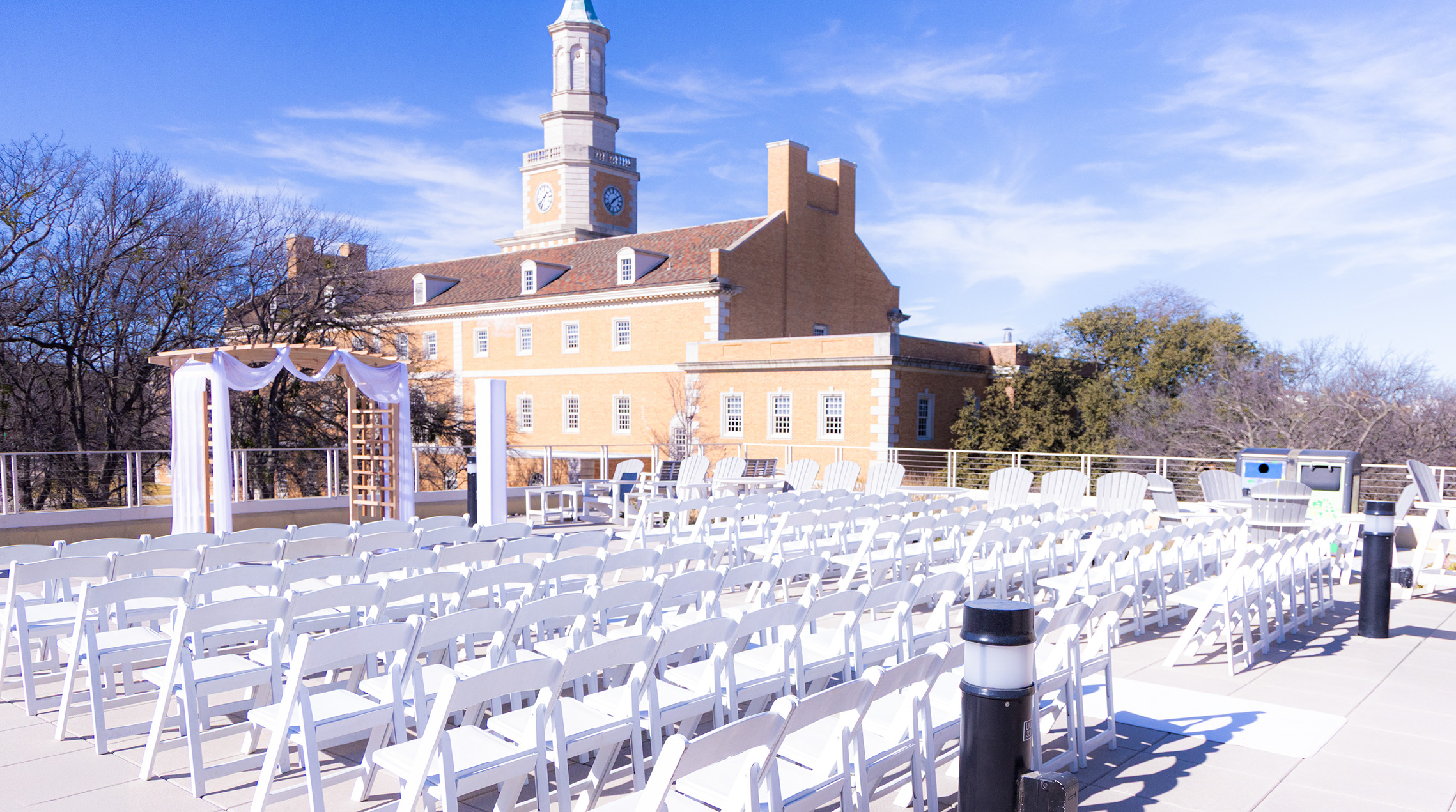Bruzzy's Patio set up for a wedding with white chairs and wedding arch on a sunny day with the Hurly building in the background.