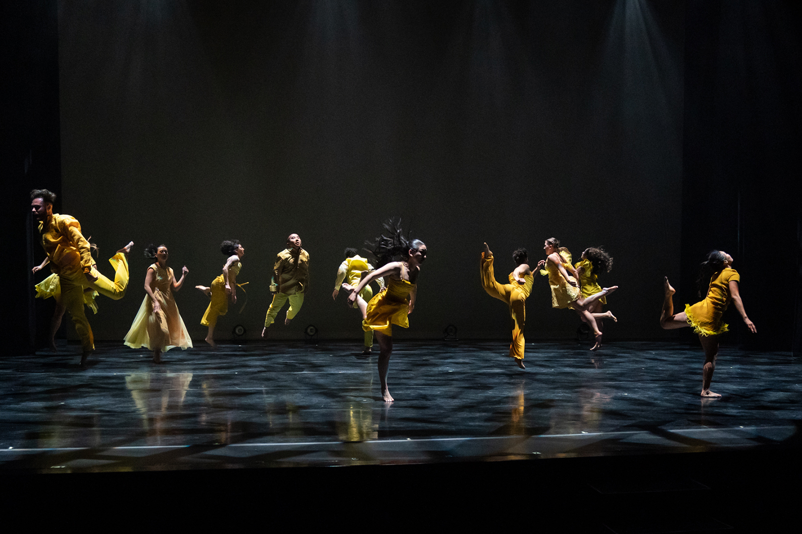 image of a dark stage with dancers in yellow costumes performing a dance routine